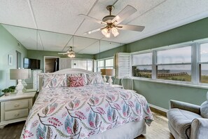 A bedroom with a bed, a ceiling fan, a TV, and a window with a view of the beach. - L1 Amelia South (Fernandina Beach)