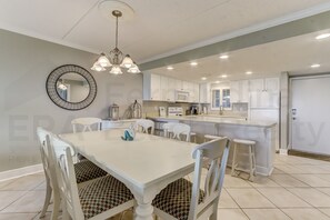 Una cocina moderna con armarios blancos, una isla central y un comedor con mesa y sillas blancas.