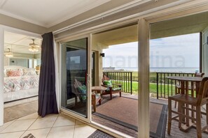 Een kamer met een schuifglazen deur die uitkomt op een balkon met zitplaatsen en uitzicht op de oceaan.