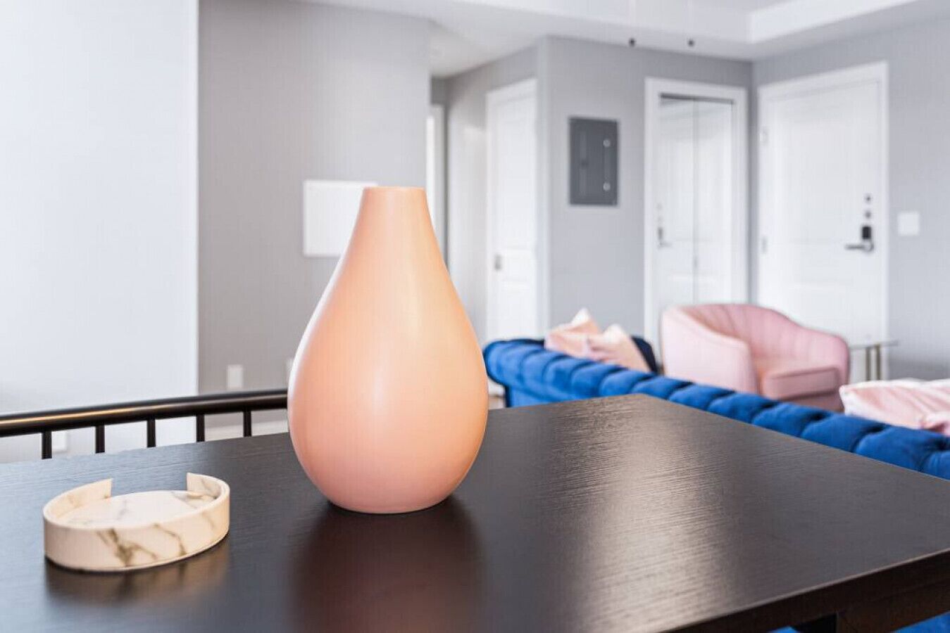 Een moderne woonkamer met een donkerhouten salontafel, een roze vaas en een marmeren onderzetter.