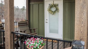 Een overdekte veranda met houten balustrade, een deur met krans, en een bloemenplanter.