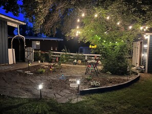 A patio area with stone flooring, a small table, chairs, and string lights.