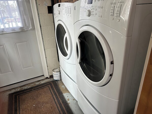 A laundry room with two front-loading washing machines, a door, and a small can of detergent on the floor. - Cozy cottage in Three Hills, Alberta. Pet Friendly! (Three Hills)