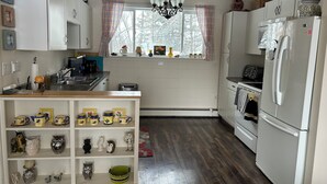 Een keuken met witte kastjes, een houten aanrecht, een kroonluchter en een raam met geruit gordijnen.
