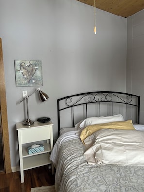 A bedroom with a bed, bedside table, lamp, and a wall art piece. - Cozy cottage in Three Hills, Alberta. Pet Friendly! (Three Hills)
