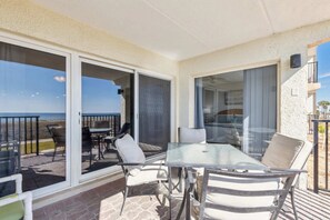 Ein Balkon mit Glastisch und Stühlen, mit Blick auf einen Strand.