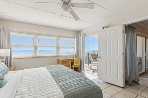 Ein Schlafzimmer mit einem Bett, einem Schreibtisch und Meerblick durch große Fenster.