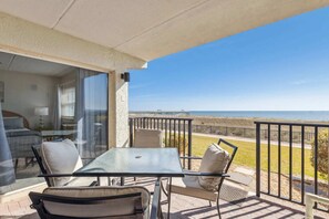A balcony with a glass door leading to a bedroom, a table with chairs, and a view of the beach. - J1 Amelia South (Fernandina Beach)