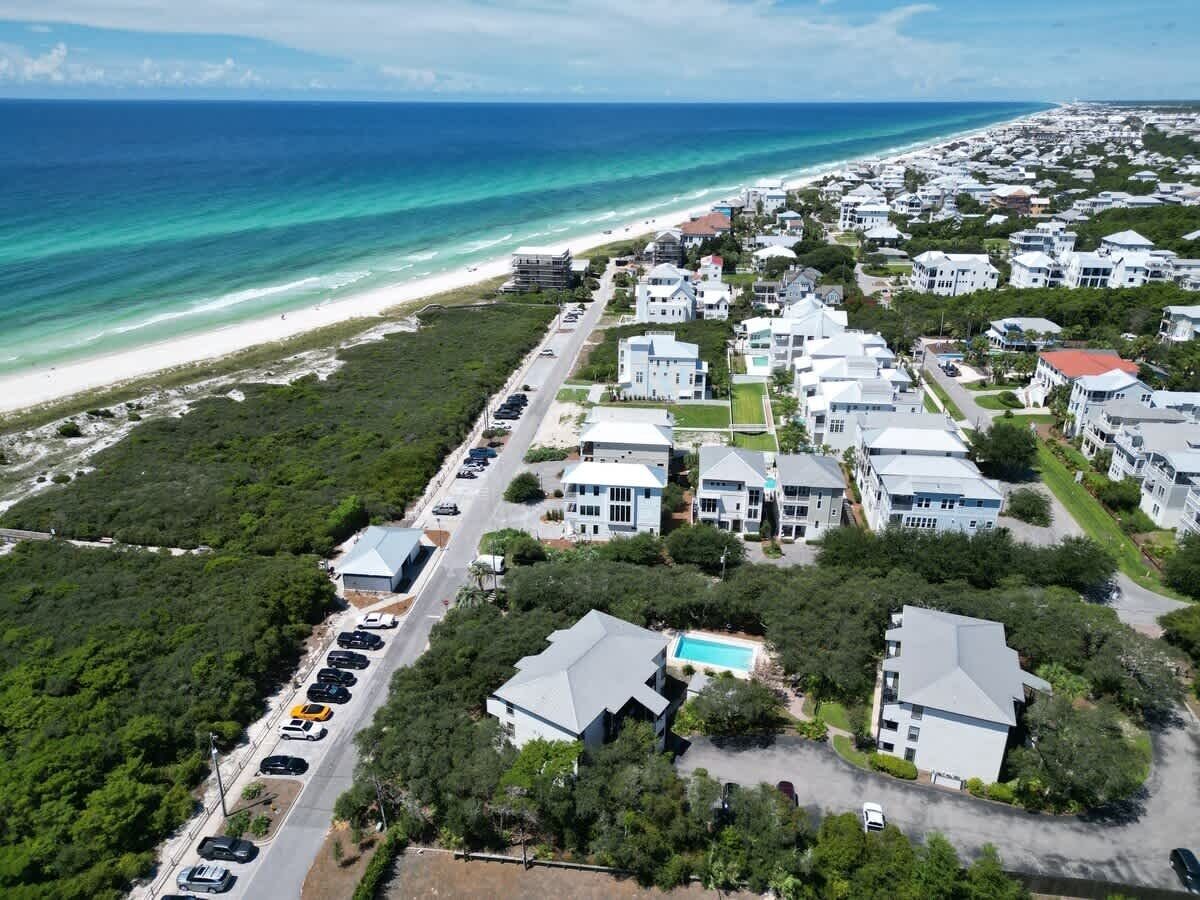 An aerial view of a coastal residential area with houses, a beach, and a clear blue ocean.