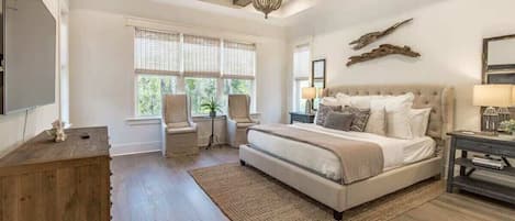 Un dormitorio con una cama grande, una araña de cristal, un aparador de madera y vistas al exterior a través de las ventanas.