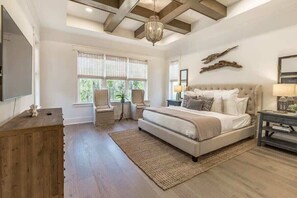 A bedroom with a large bed, a chandelier, a wooden dresser, and a view of the outdoors through the windows. - Castaway at Seagrove – Luxury NatureWalk Retreat (Santa Rosa Beach)