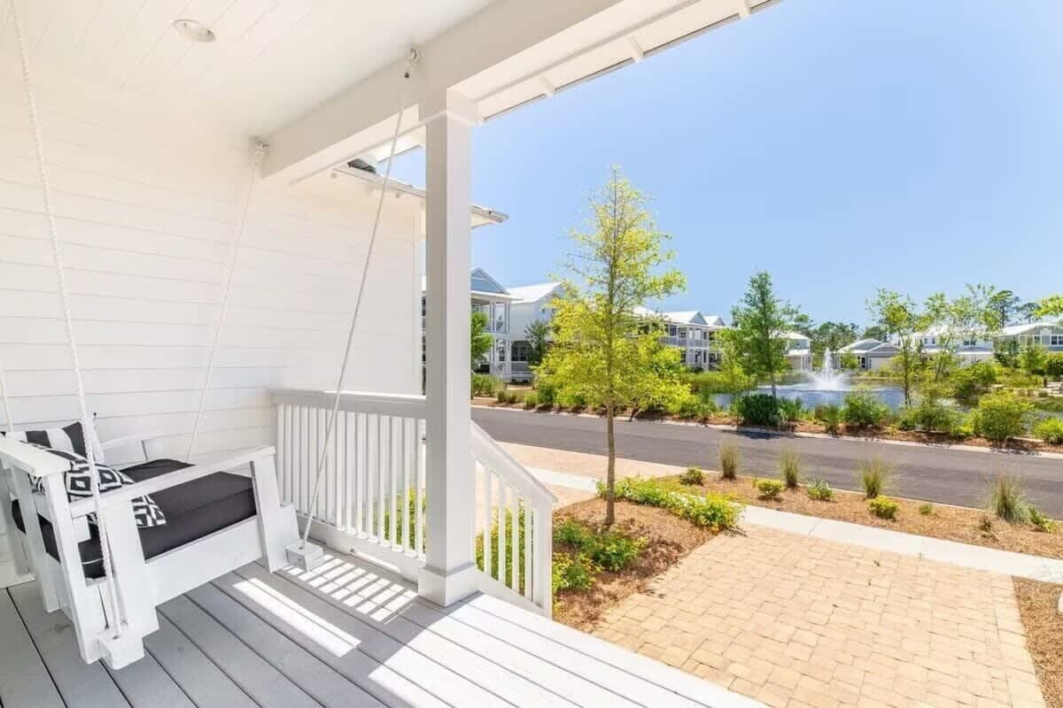 A white porch with a swing seat, a view of a residential street, and a clear sky.