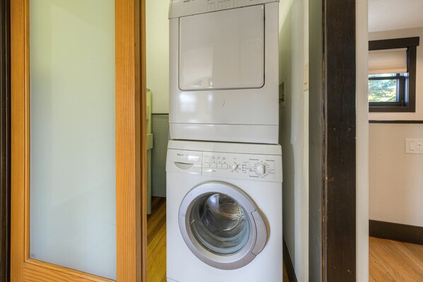Eine Waschmaschine mit Frontlader in einem Waschraum, mit einem Holztürrahmen und einem Fenster über der Maschine.