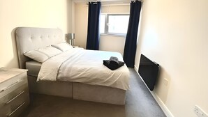 Camera da letto con un letto, comodino, lampada e finestra con tende.