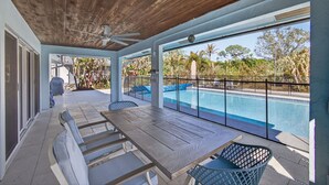 Un espace extérieur abrité, doté d’une piscine, d’une table en bois et de chaises, et offrant une vue sur une autre piscine et sur la verdure.