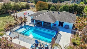 Une maison dotée d’une grande piscine, d’un patio couvert avec des chaises longues et d’un jardin bien entretenu.