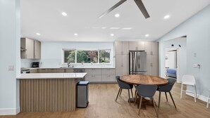 Une cuisine moderne dotée d’un îlot central, d’un coin repas avec une table ronde et d’un ventilateur de plafond.