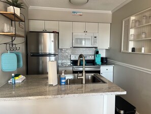 A kitchen with white cabinets, stainless steel appliances, a granite countertop, and a small island with a sink. - Oceanfront Villa-Beachfront Heated Pool-Walk to Coligny Plaza-South Forest Beach (Hilton Head Island)