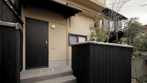 A residential building with a dark wooden door, beige walls, and a small set of steps leading to a balcony. - Nozomu House02 (Kyoto)