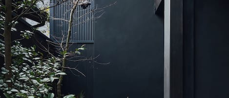 Un espacio exterior moderno con una pared oscura, una pequeña zona de estar y abundante vegetación.
