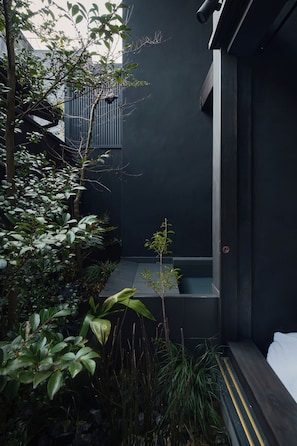 A modern outdoor space with a dark wall, a small seating area, and lush greenery. - Nozomu House02 (Kyoto)