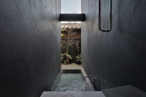 Une salle de bain étroite et moderne, dotée d’une baignoire intégrée, d’un robinet apparent et d’une petite fenêtre en hauteur.