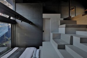 Un interior moderno con una cama, una escalera y un ventanal con vistas a un jardín.