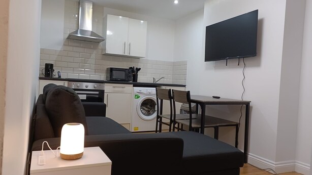 A compact living space with a kitchenette, a washing machine, a dining area, and a flat-screen TV mounted on the wall. - Cosy Central Cardiff Retreat (Cardiff)