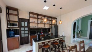 A kitchen with a central island, bar stools, a microwave, and a refrigerator. - Casa Kaax - by Kanaa (Mérida)