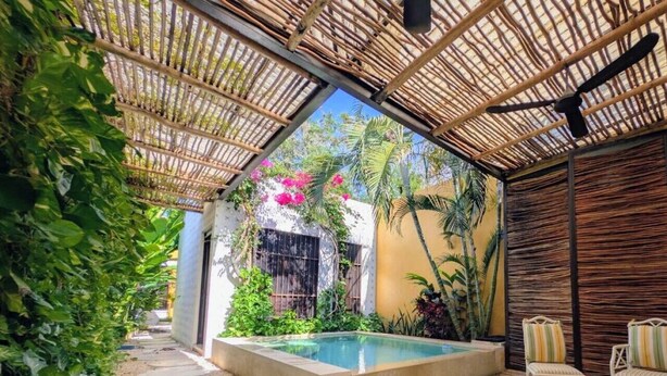 A pool area with a bamboo roof, surrounded by greenery and a small seating area. - Casa Kaax - by Kanaa (Mérida)