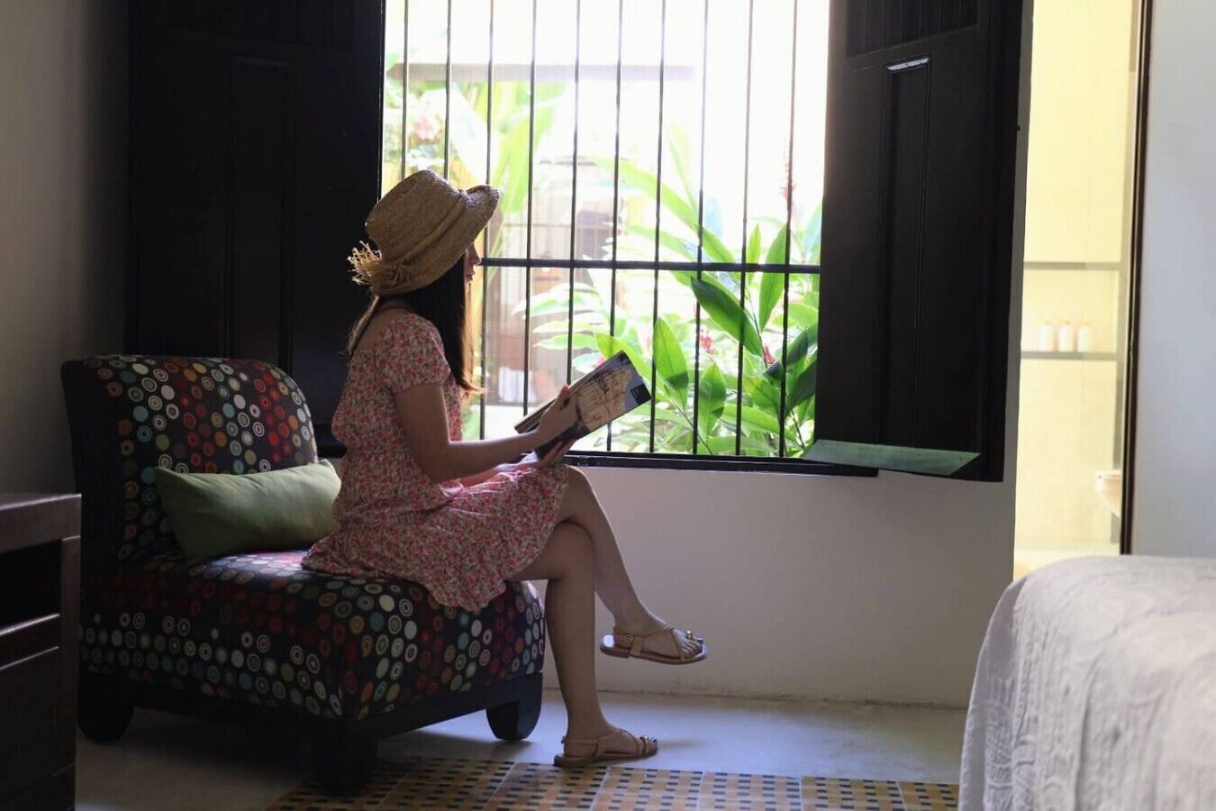 A person sitting on a patterned chair by a window with a view of greenery.