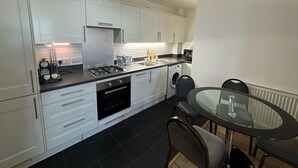 A modern kitchen with white cabinets, a gas stove, a built-in oven, a washing machine, and a dining table with chairs. - 4 Bed 2 Bath Balcony Retreat - 15min-O2 Arena! (London)