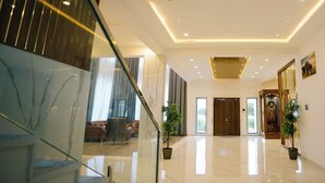 Un lobby espacioso con piso de mármol, una escalera y una zona de estar con sofá y cortinas.