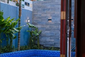 A swimming pool with blue tiles, a stone wall, and potted plants. - Sila Ananda 6BRs Pool Villa Dao Xanh Island Da Nang (Da Nang)