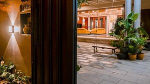 An entrance with a wooden door, a tiled patio with potted plants, and a reception area with yellow seating and a bench. - Sila Ananda 6BRs Pool Villa Dao Xanh Island Da Nang (Da Nang)