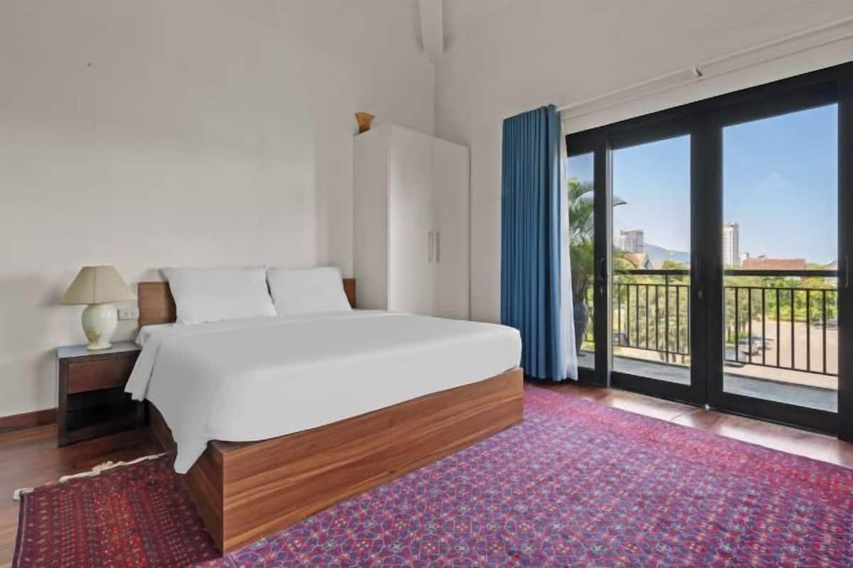 A bedroom with a wooden bed, a nightstand, a white wardrobe, and a balcony with blue curtains.