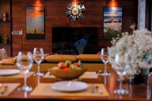 Un comedor con chimenea, un sofá y una mesa preparada para dos personas, con copas de vino y un frutero.
