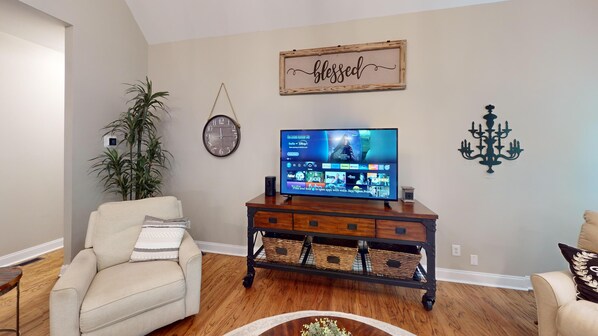 Un salon comprenant un téléviseur, une horloge, un panneau fixé au mur, une plante et un lustre.