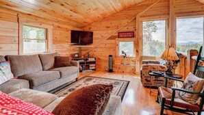 A cozy cabin interior with a wooden ceiling, a flat-screen TV, a sofa, a patterned armchair, and a rug. - 489oer (Whitefield)