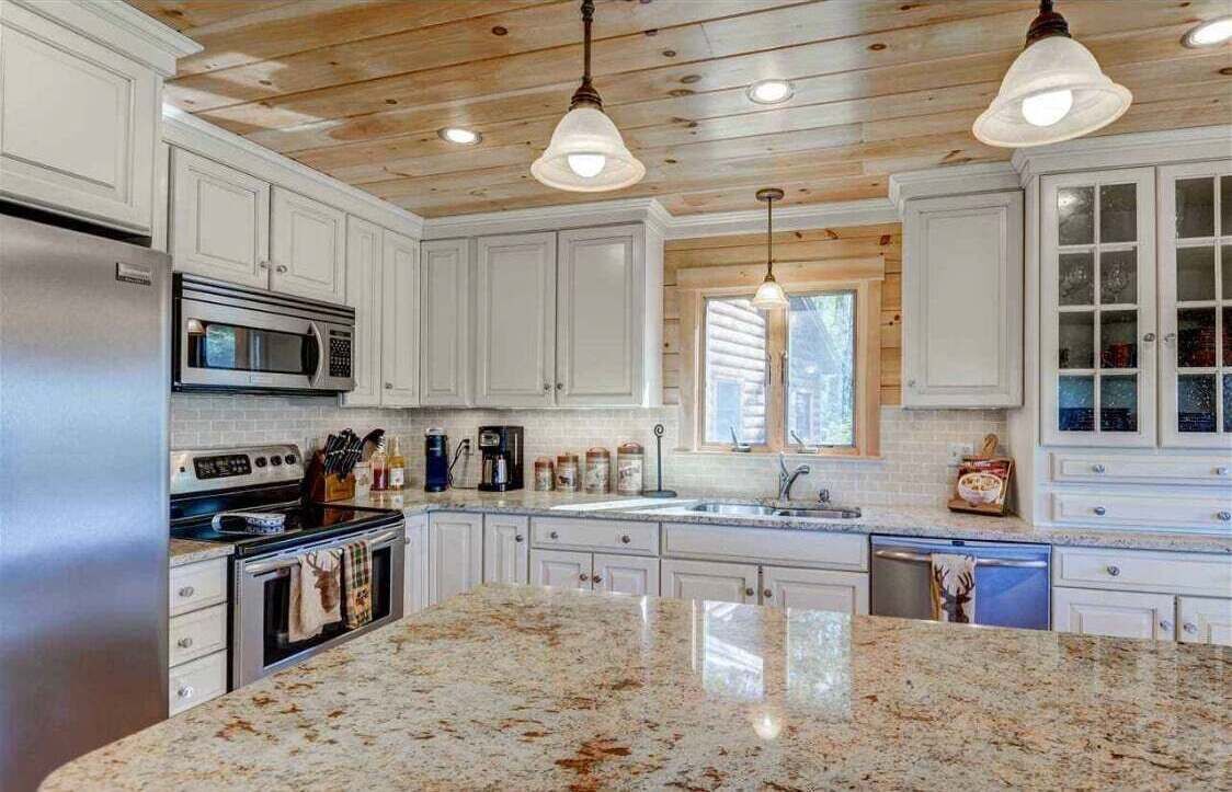 A kitchen with white cabinets, a granite countertop, stainless steel appliances, and wooden ceiling beams.