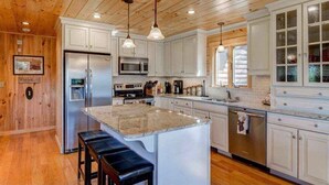 A kitchen with wooden ceiling, white cabinets, stainless steel appliances, and a granite island. - 489oer (Whitefield)