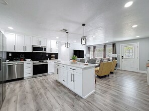 Een moderne keuken met witte kasten, een centraal eiland, roestvrijstalen apparatuur en een houten vloer.