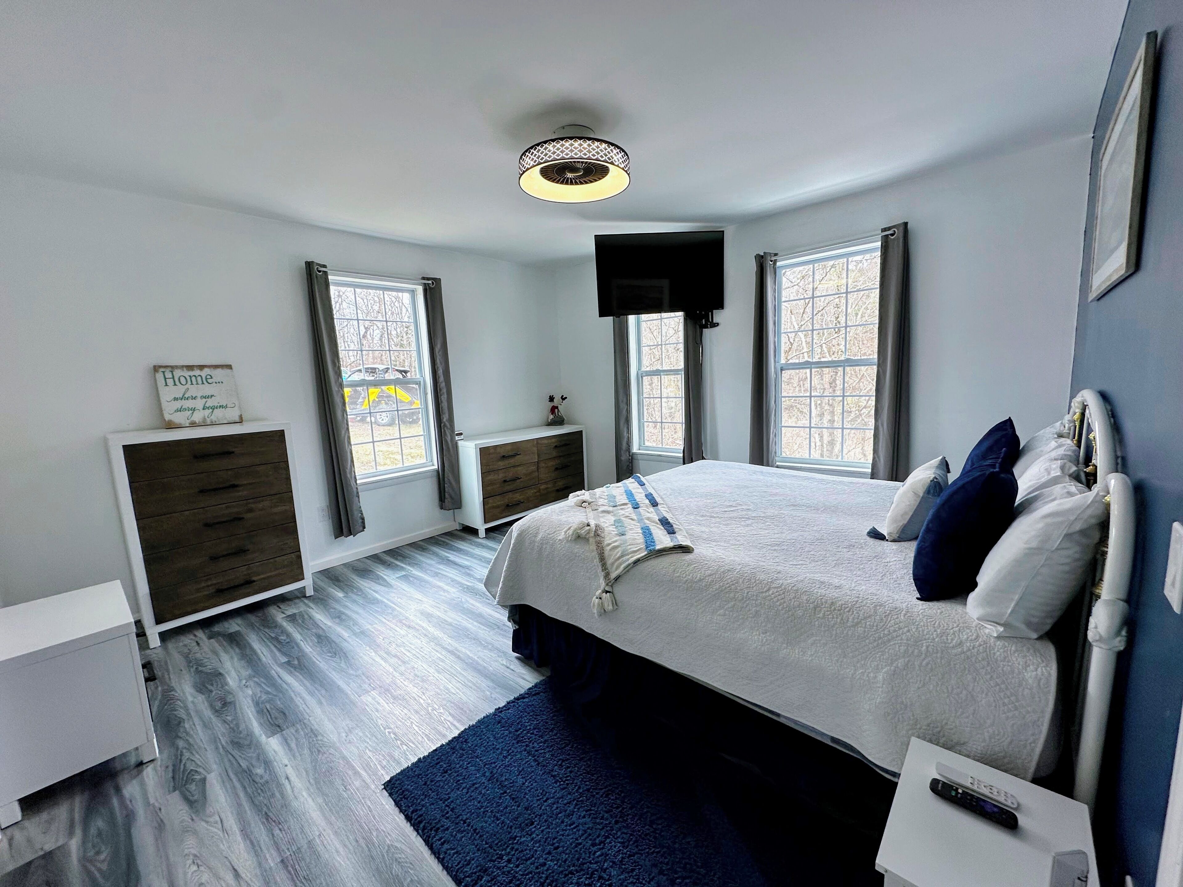 A modern bedroom with a bed, bedside tables, a dresser, and a ceiling light.