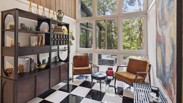 A room with a large window, a checkered floor, two armchairs, a small table, and a bookshelf. - Pineview Haven (Knoxville)