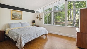 A bedroom with a large window, a bed, a nightstand, and a painting on the wall. - Pineview Haven (Knoxville)