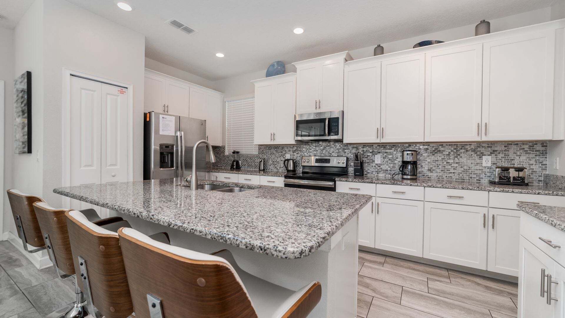 A modern kitchen with white cabinets, granite countertops, stainless steel appliances, and a breakfast bar with bar stools.