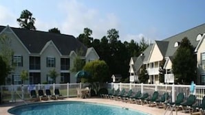 A swimming pool with a curved edge, surrounded by a white fence, and adjacent to a row of green lounge chairs. - Village at the Glens G 109 (Little River)
