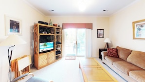 A living room with a television, a sofa, a bookshelf, and a dining area with chairs. - Village at the Glens G 109 (Little River)