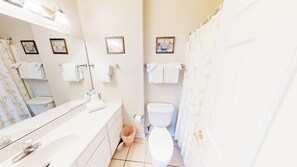 A bathroom with a white sink, mirror, toilet, and shower curtain. There are towels hanging on the wall and a basket on the floor. - Village at the Glens G 109 (Little River)