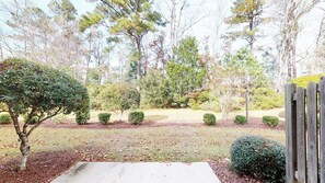 A landscaped garden with a variety of trees and shrubs, a wooden fence, and a concrete path. - Village at the Glens H 110 (Little River)